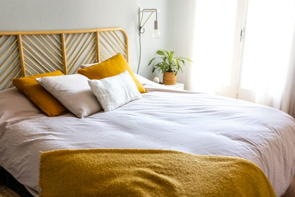 Light and airy cozy bedroom with bed, lamps, cushions and plant. No people. Home interior